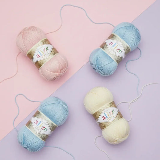 Cuatro ovillos de hilo Alize Diva de microfibra acrílica sedosa en tonos pastel: rosa, dos azul claro y amarillo cremoso.