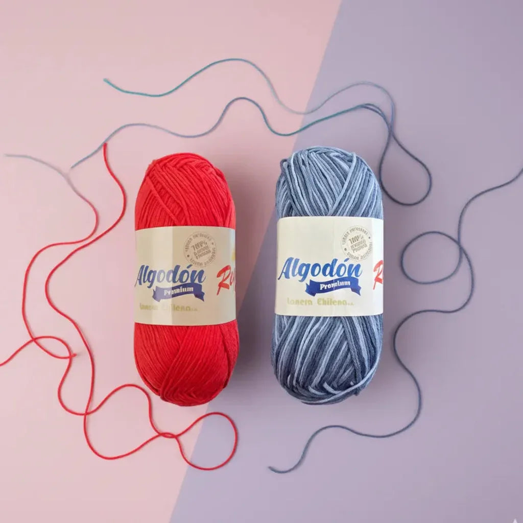 Dos ovillos de hilo Algodón Premium Reginella, uno rojo intenso y otro gris matizado, sobre fondo bicolor con hilos sueltos.