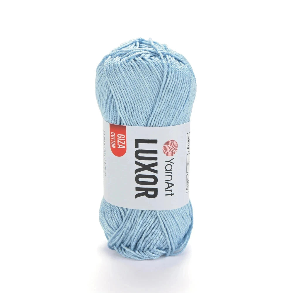 Ovillo de hilo YarnArt Luxor de algodón mercerizado Giza color celeste claro sobre fondo blanco.