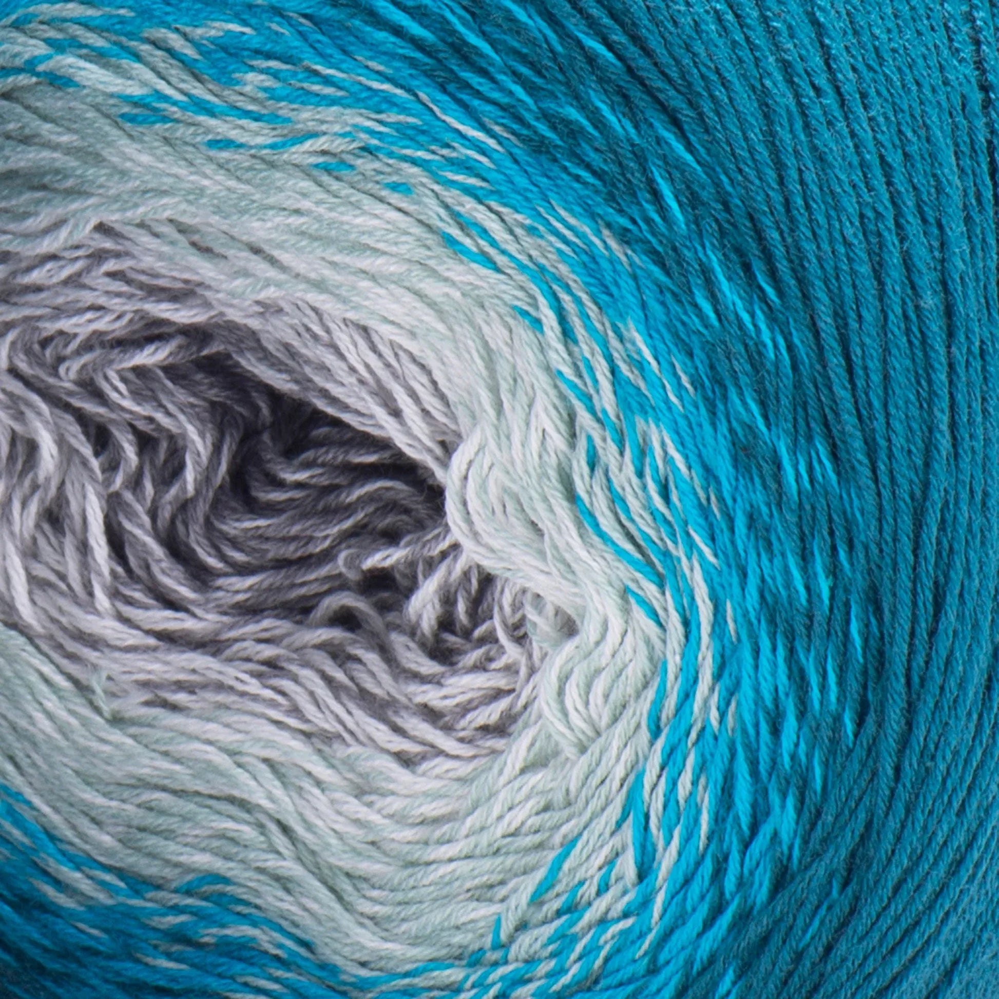 Ovillo de lana degradé en tonos azul turquesa, gris claro y gris oscuro. Hilo de algodón acrílico texturizado.