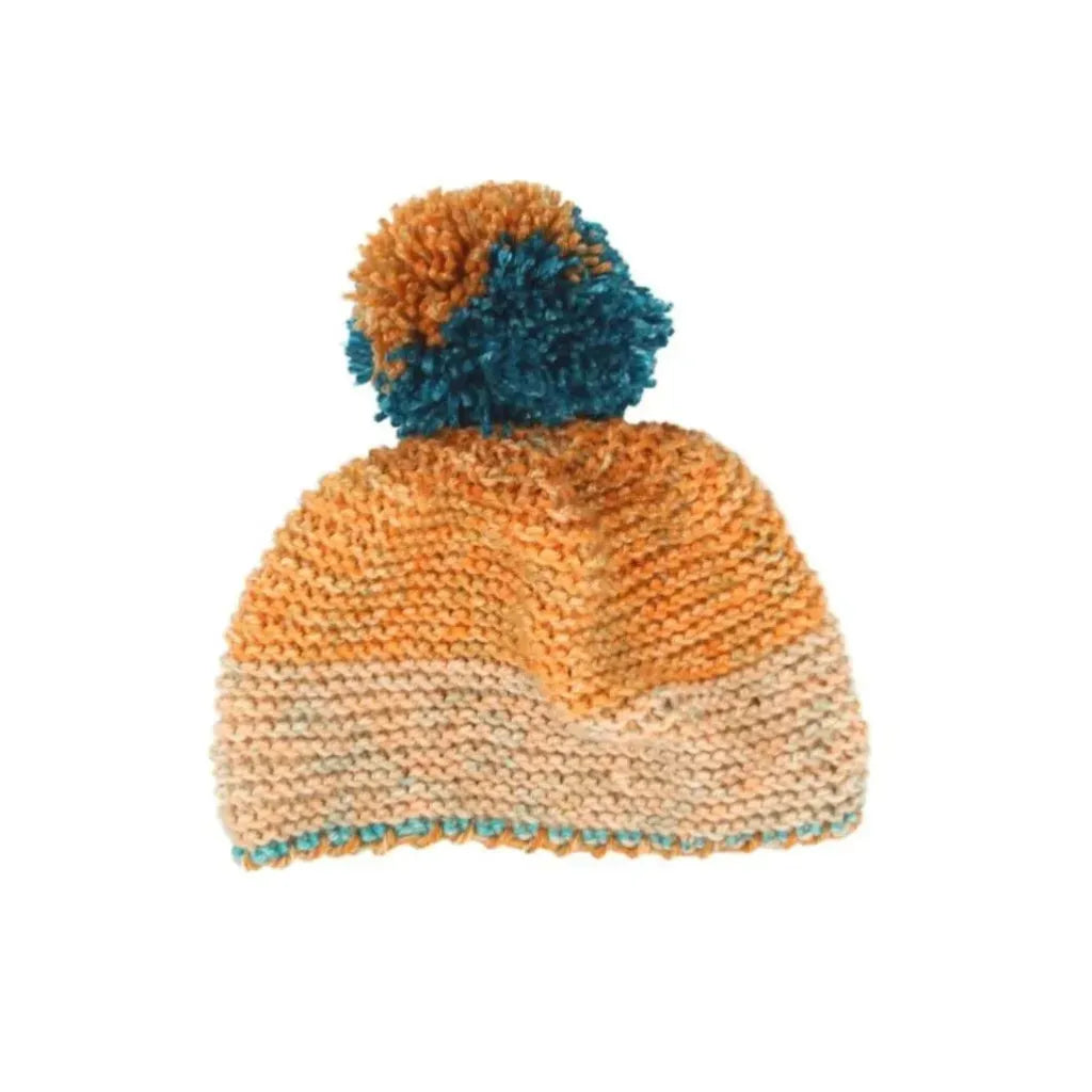 Gorro de bebé tejido a mano con pompom, 100% acrílico, en tonos naranja, beige y azul turquesa. Suave e hipoalergénico.