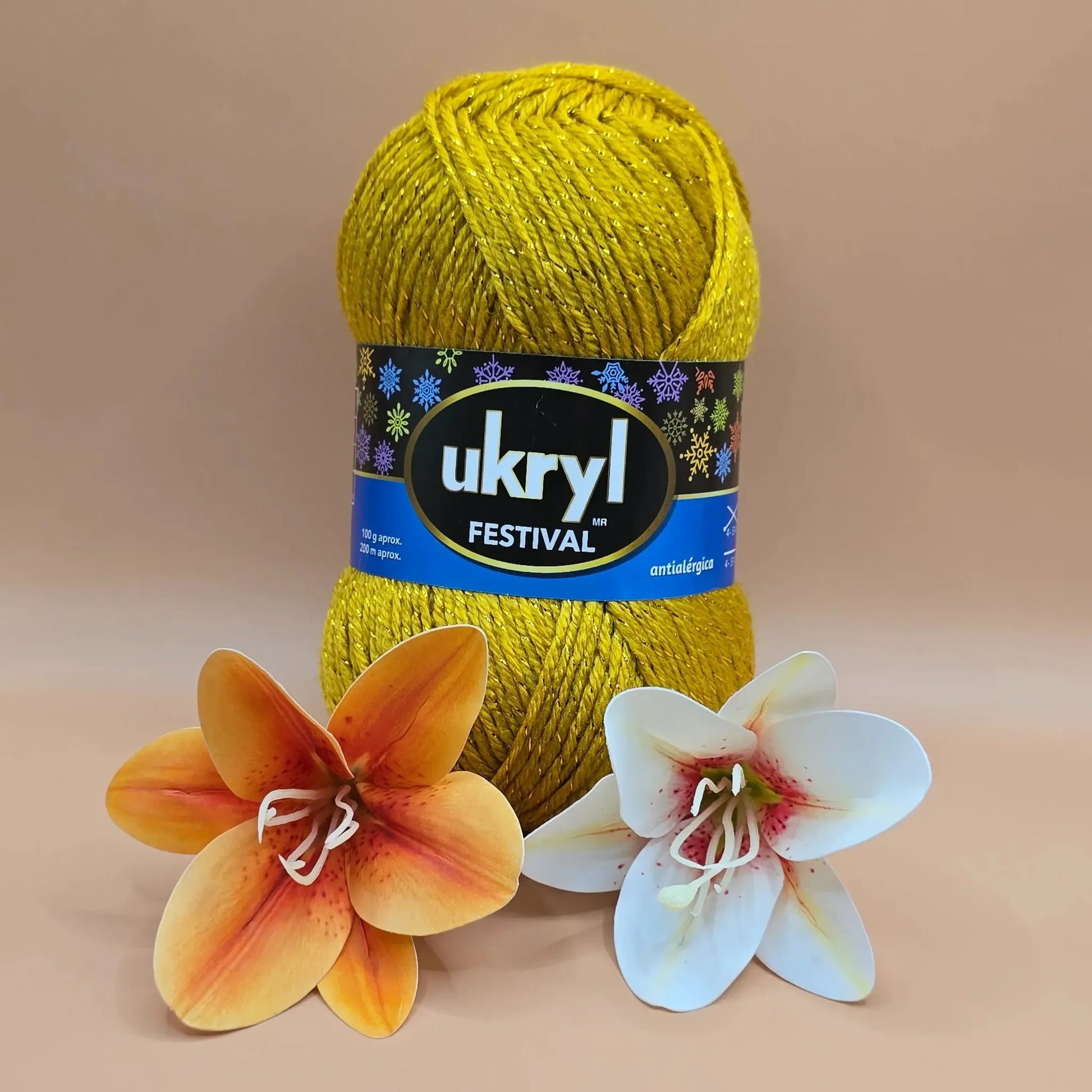 Ovillo de lana Ukryl Festival acrílico brillante dorado con lurex, antiálérgica, junto a flores decorativas.