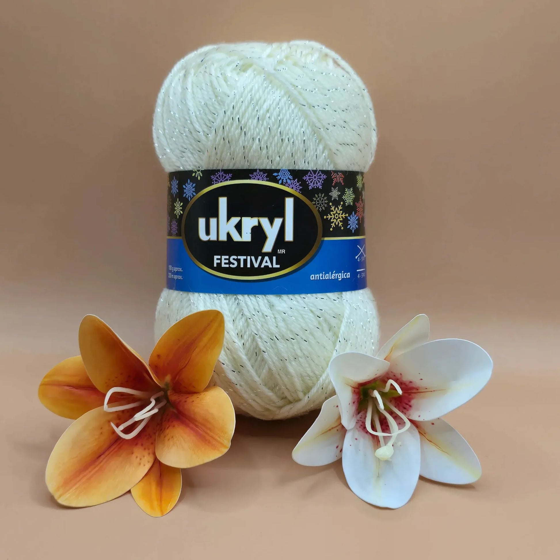 Ovillo de lana Ukryl Festival acrílico color crema brillante con lurex plateado, junto a flores decorativas.