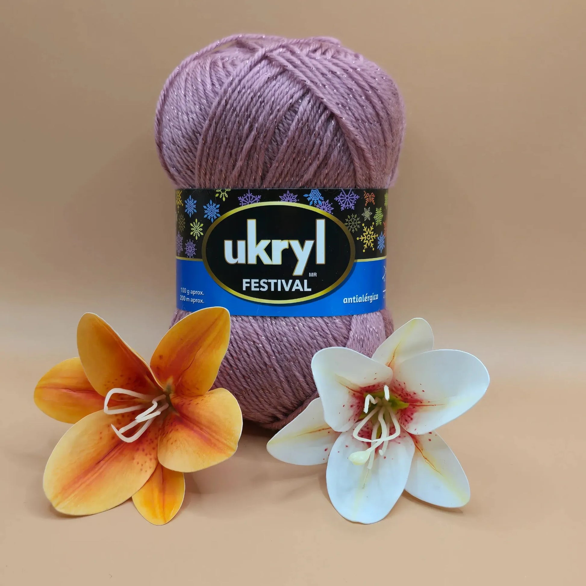 Ovillo de lana Ukryl Festival lila brillante con lurex, 94% acrílico antialérgico, junto a flores decorativas.