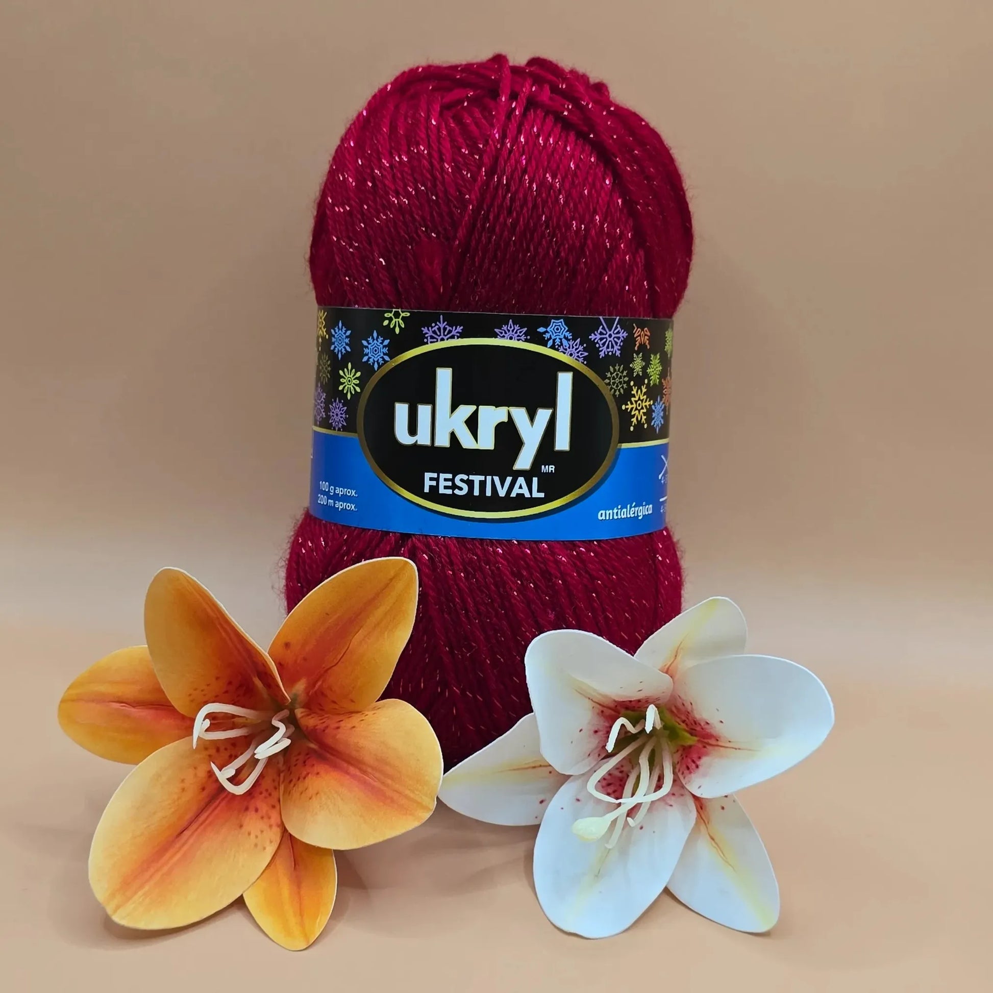 Ovillo de lana Ukryl Festival rojo brillante con destellos de lurex. Hilo 94% acrílico, 6% lurex, antialérgico, junto a dos flores decorativas.