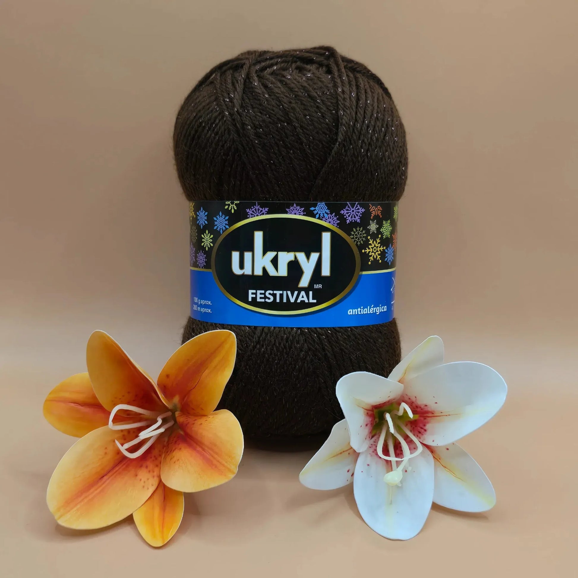 Ovillo de lana Ukryl Festival color café oscuro con brillos de lurex, 94% acrílico antialérgico, junto a dos flores.