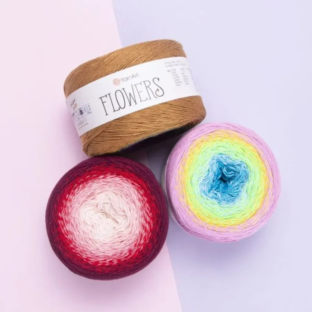 Tres ovillos de lana YarnArt Flowers: uno marron solido, uno degrade rojo-rosa-blanco y otro multicolor pastel. Hilos de algodon acrilico.