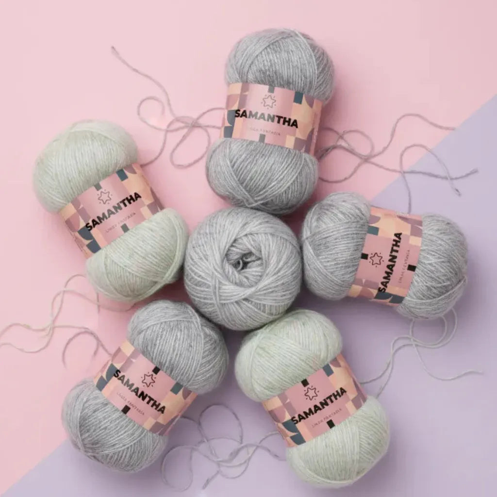 Seis ovillos de hilo Samantha Reginella 100% poliéster matizado en tonos gris y verde claro, sobre fondo rosa y lila.